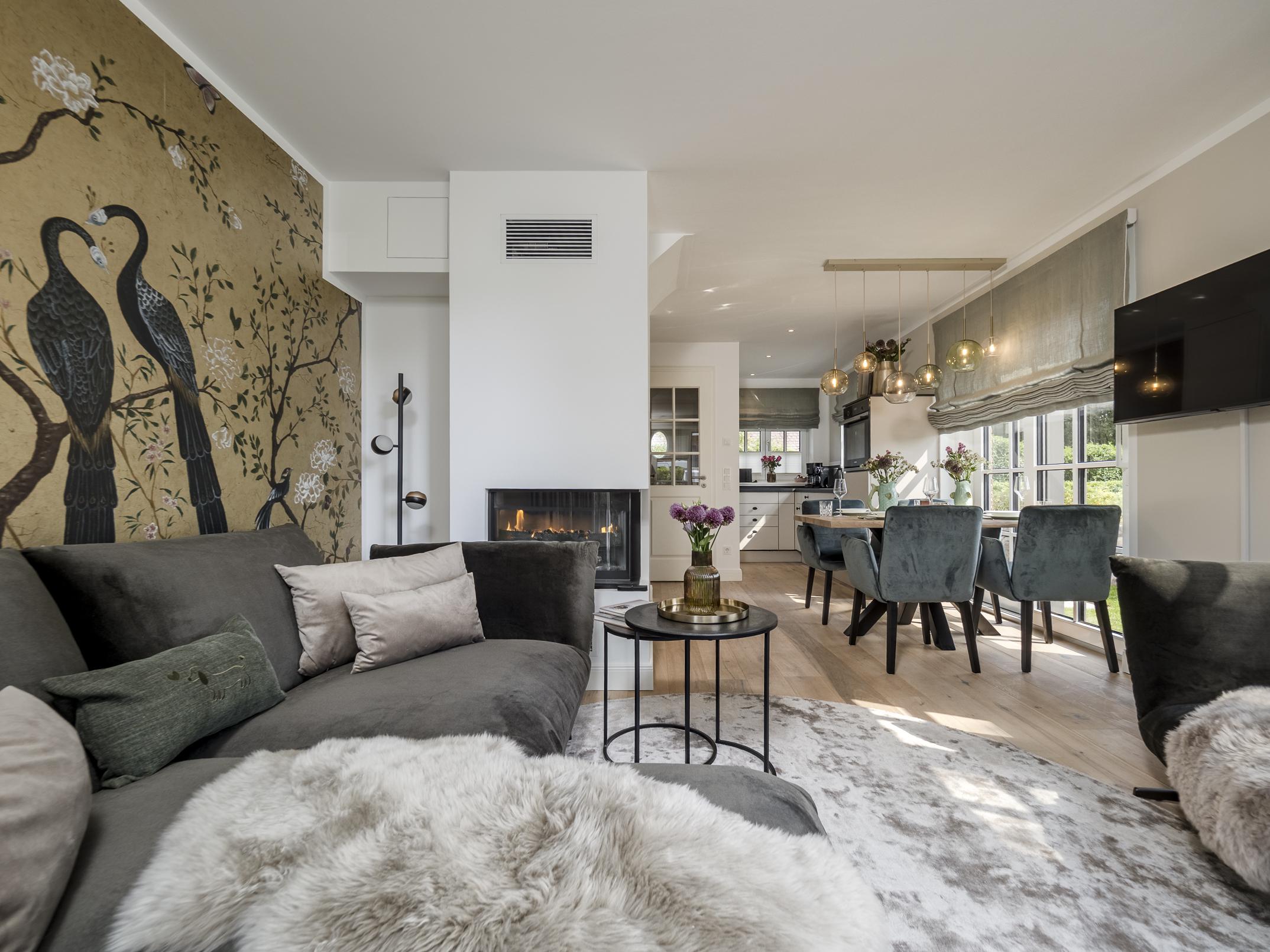 Offener Wohn- und Essbereich der Ferienwohnung 'Greta & Sylt' mit gemütlichem Kamin, Designer-Tapete und stilvoller Einrichtung.