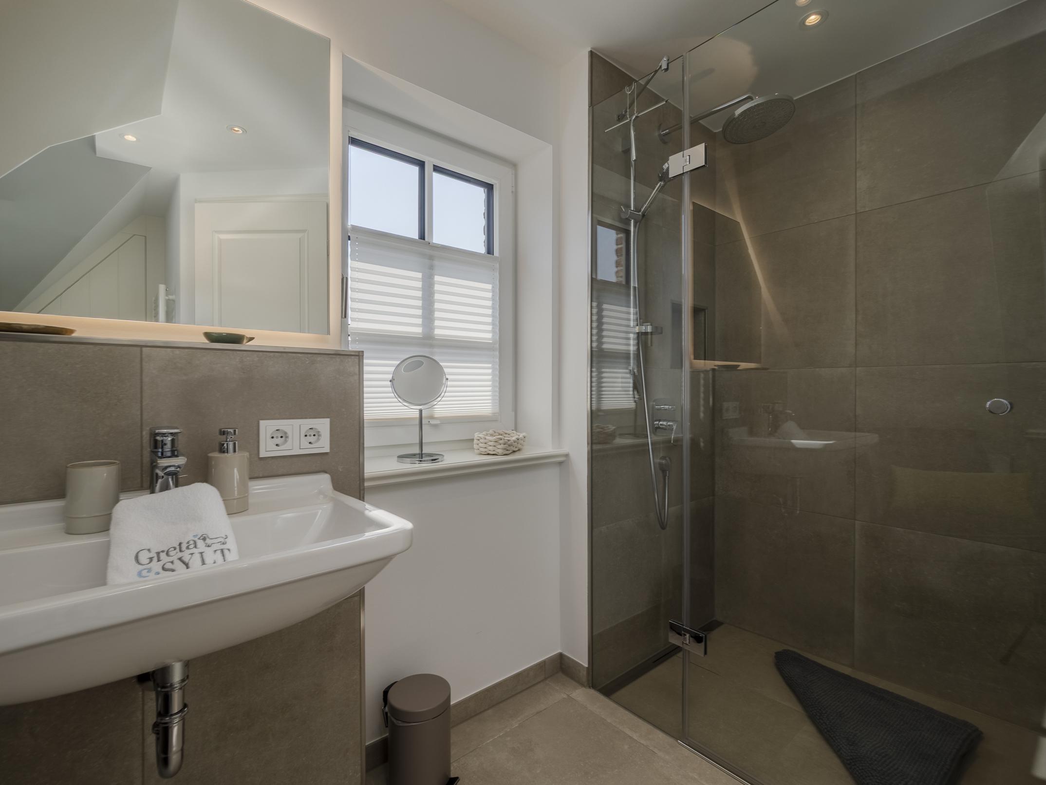 Modernes Badezimmer der Ferienwohnung 'Greta & Sylt' mit bodengleicher Dusche und hochwertiger Ausstattung.