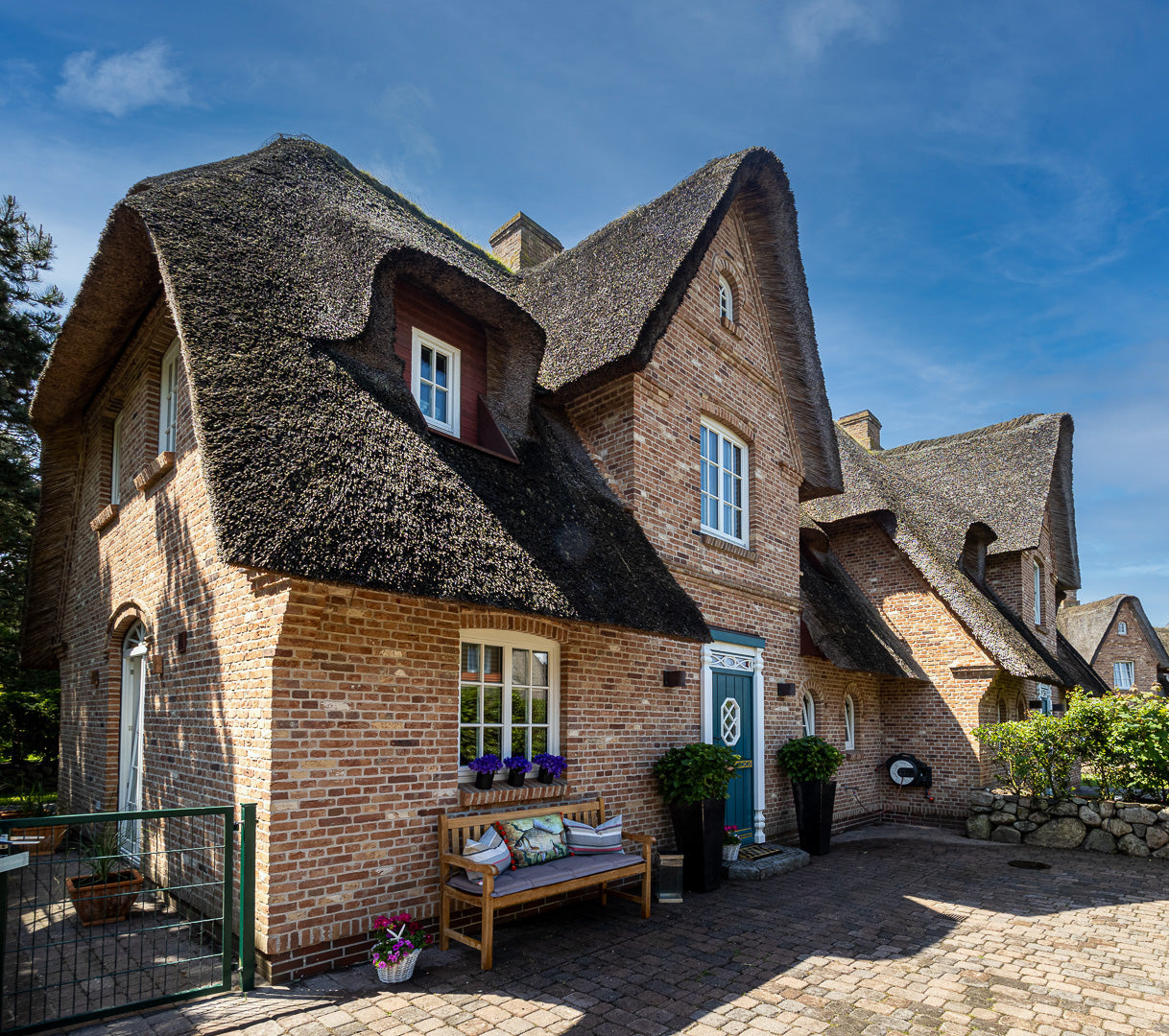 Traditionelles Reetdachhaus mit Backsteinfassade und gemütlicher Holzbank vor dem Eingang, rein dekorativ.