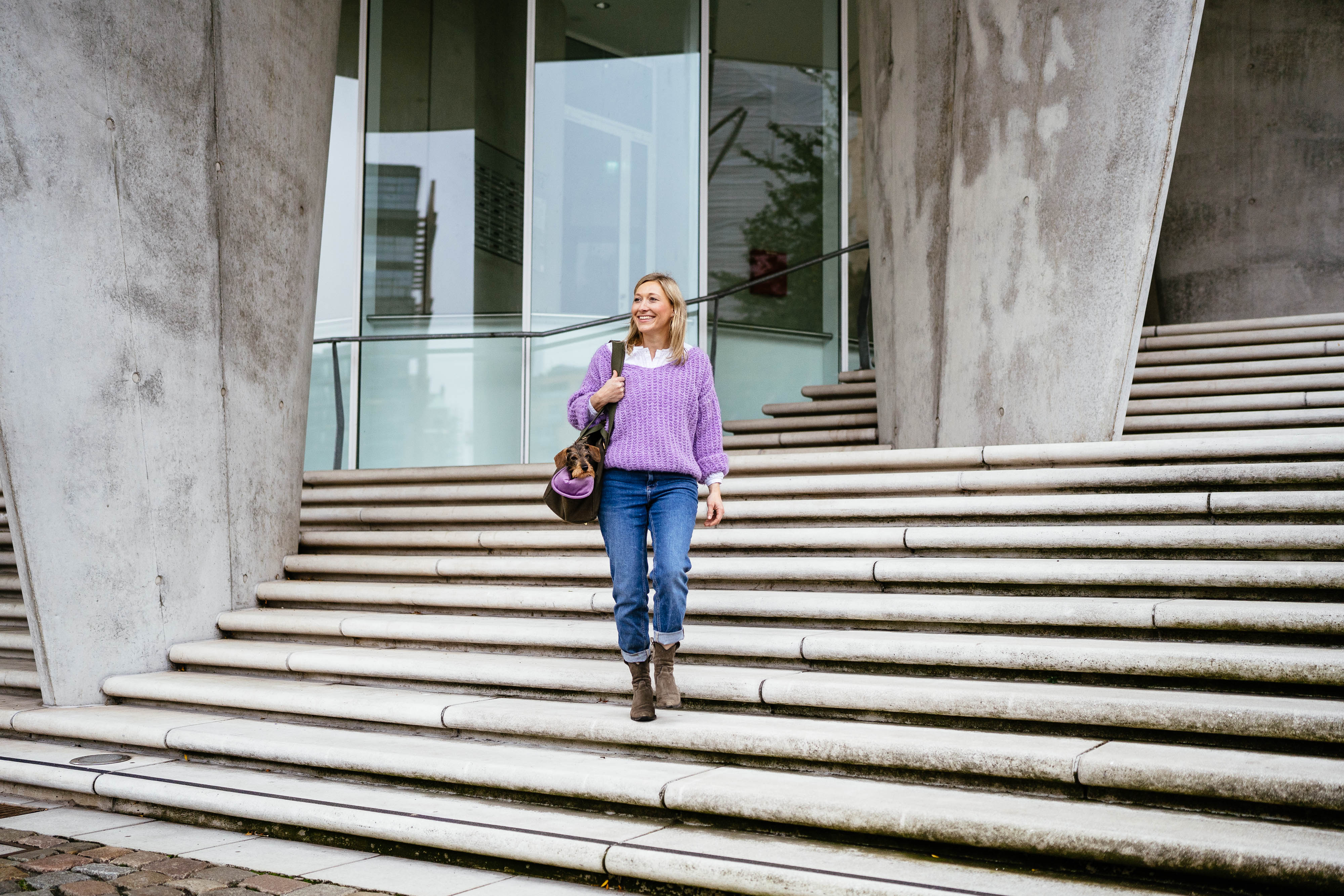 Julia geht eine moderne Betontreppe in Hamburg hinunter und trägt ihre Dackeldame Gretchen in einer khakifarbenen, handgefertigten Hundetasche von Greta & PAUL.