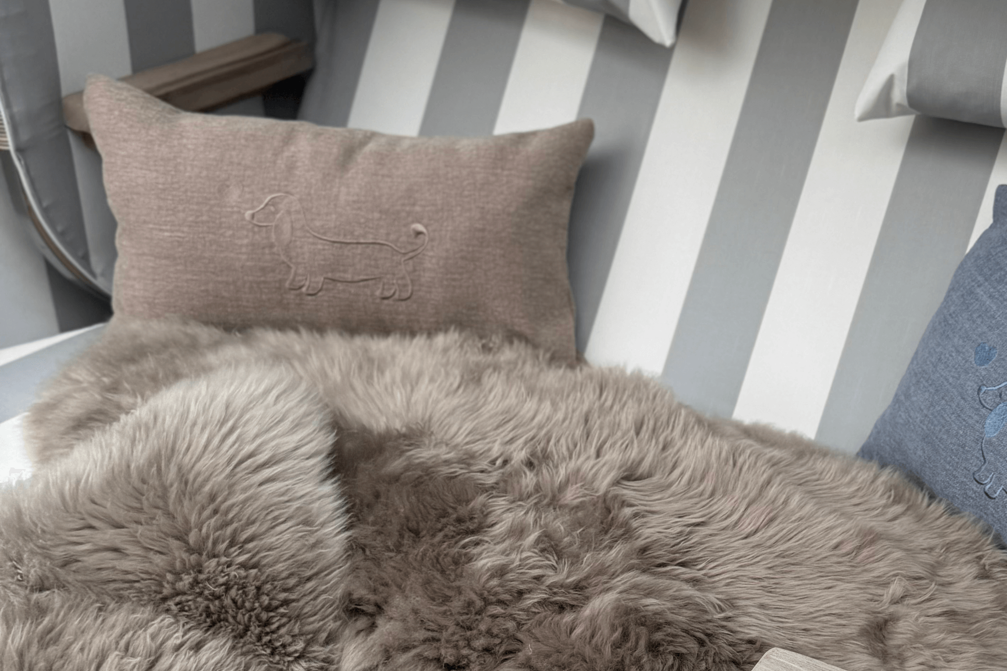 Greta & PAUL Leinen-Kissen in Hellbeige mit Dackel-Stickerei, stilvoll auf einem flauschigen Fell in einem Strandkorb arrangiert.