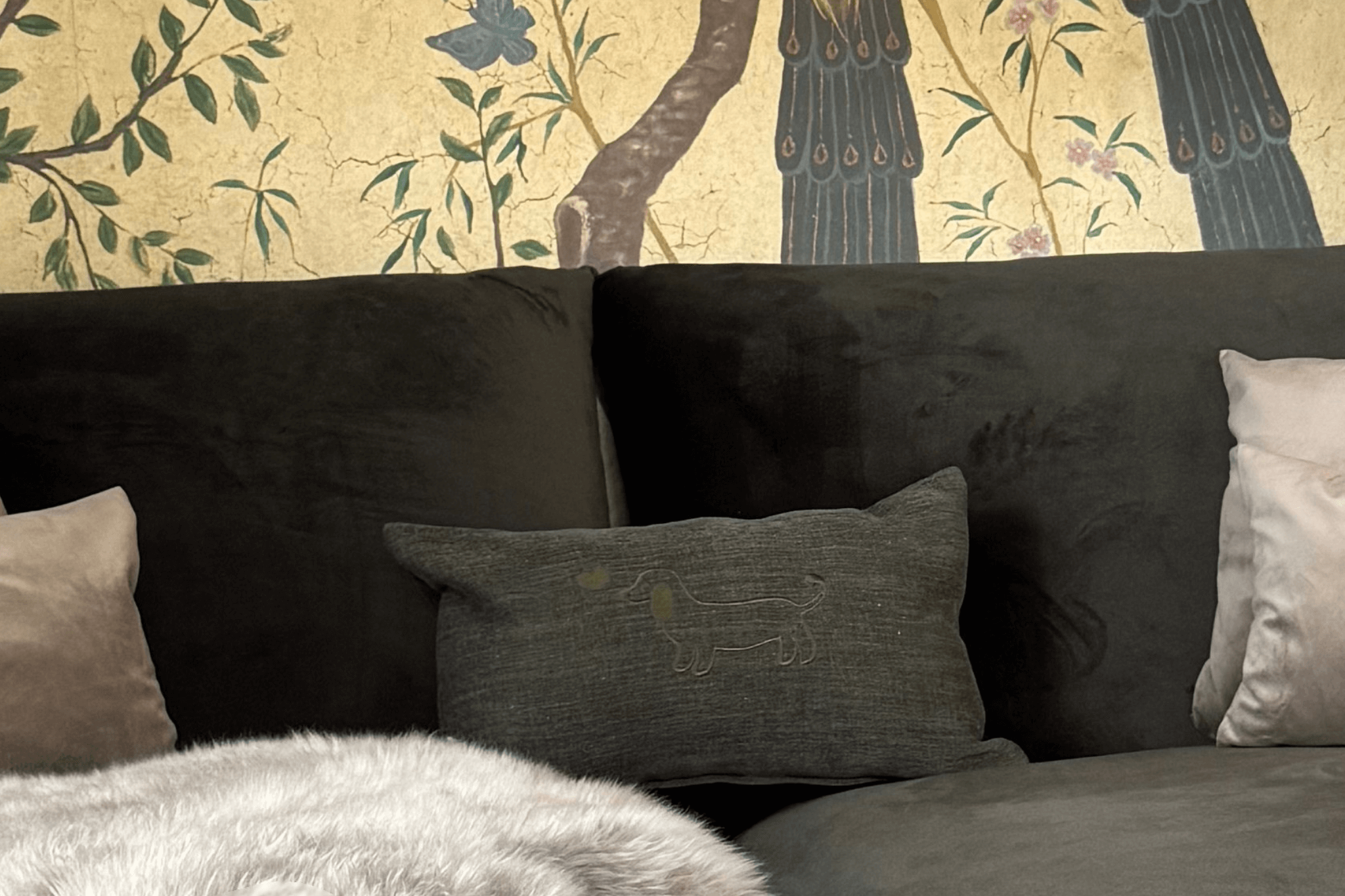 Greta & PAUL Leinen-Kissen in Olivgrün mit Dackel-Stickerei, gemütlich auf einer dunklen Samtcouch arrangiert.