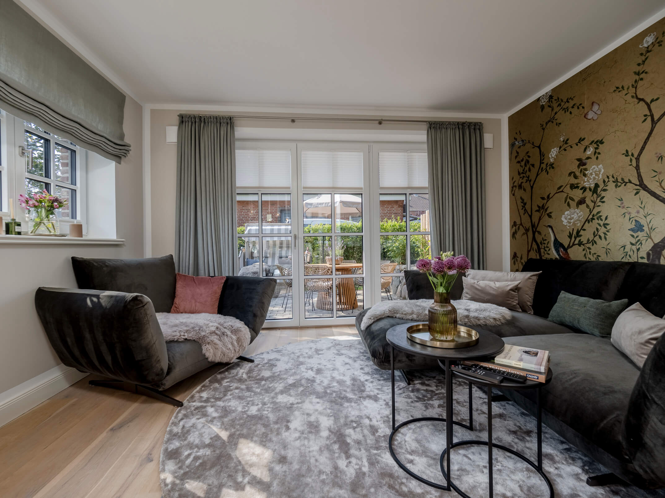 Der Wohnbereich der Ferienwohnung 'Greta & Sylt' mit großer Couch, Designer-Tapete und direktem Zugang zur sonnigen Terrasse.