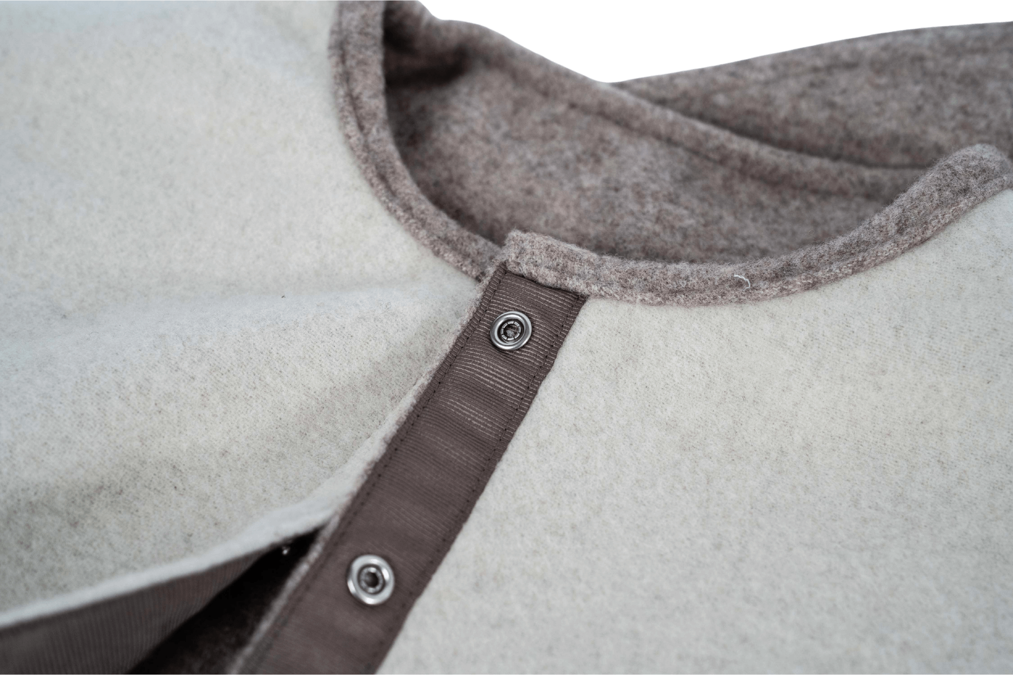 Detailaufnahme der Druckknöpfe und des Verschlussbands des Wendecapes Gretchen Couture in Beige-WollweiĂ.