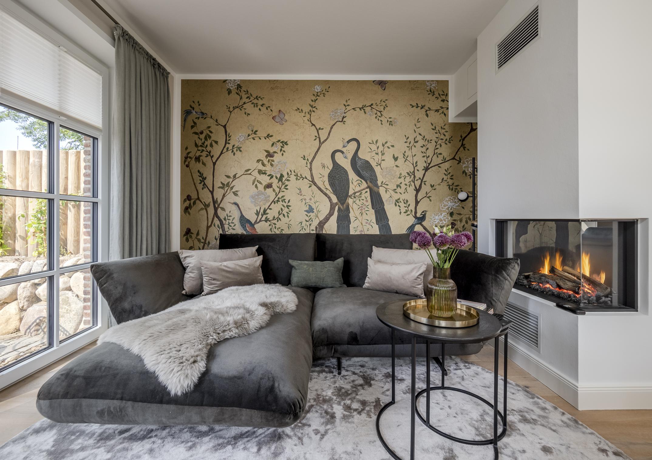 Gemütliches Wohnzimmer mit Kaminfeuer, großer Couch und stilvoller Designer-Tapete.
