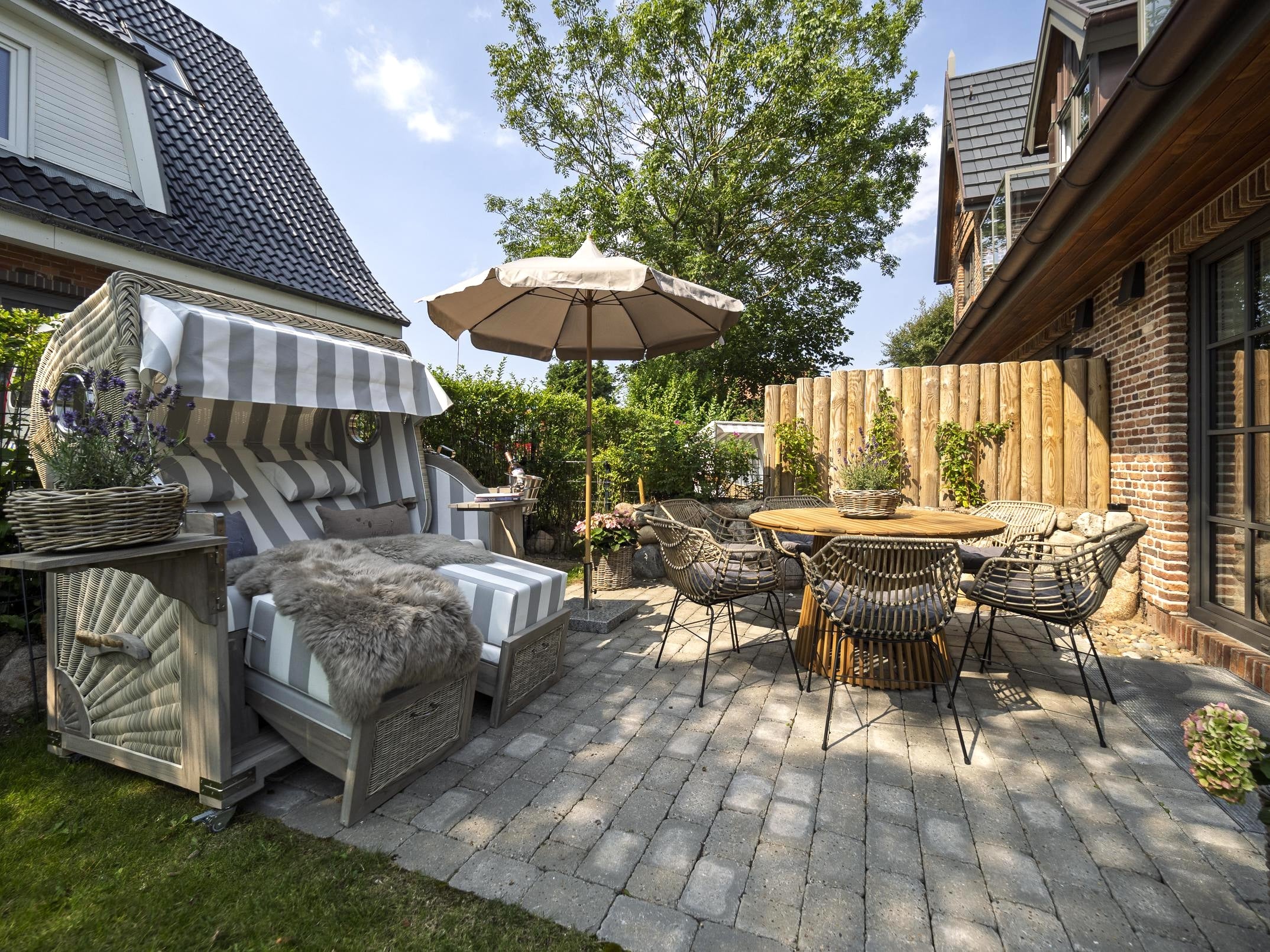 Sonnige Terrasse der Ferienwohnung 'Greta & Sylt' mit gemütlichem Strandkorb und stilvollem Essbereich.
