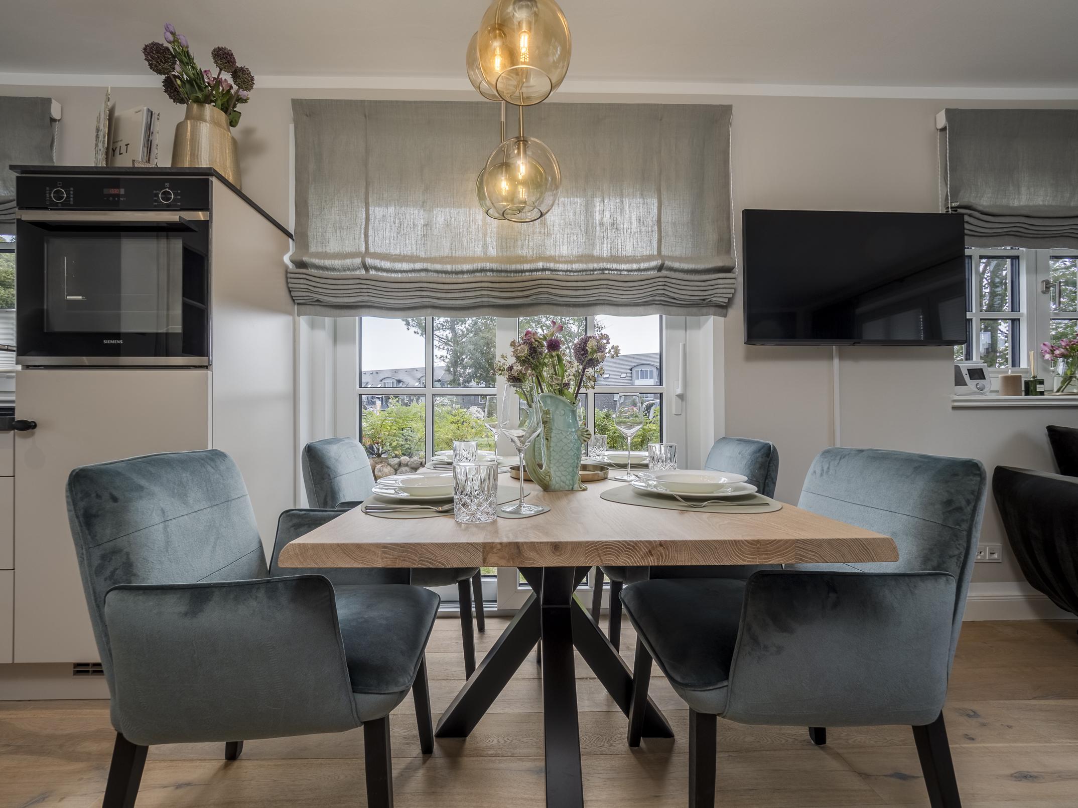 Der einladende Essbereich der Ferienwohnung 'Greta & Sylt' mit gedecktem Tisch und moderner, offener Küche.
