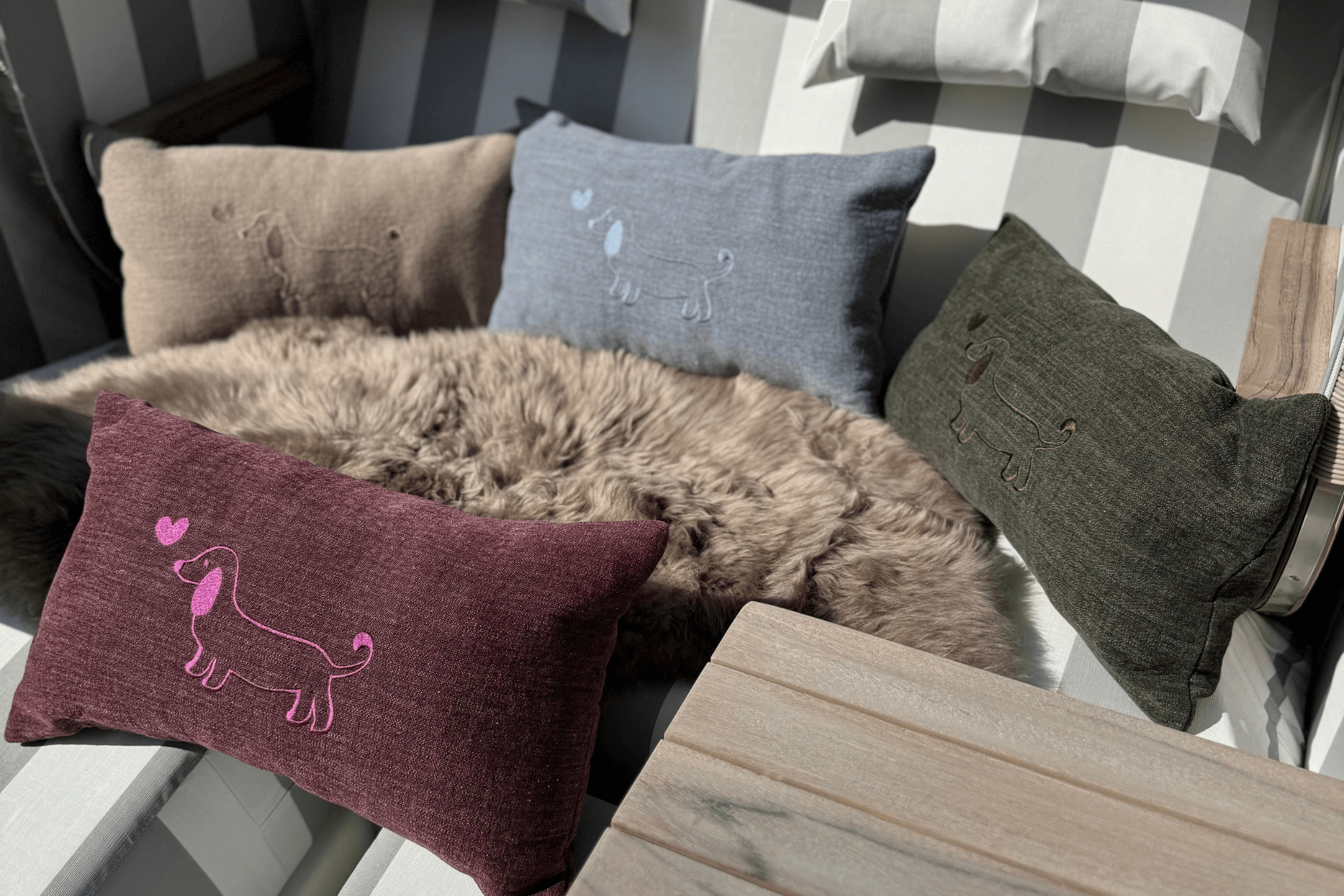 Die Kollektion der Greta & PAUL Leinen-Kissen mit Dackel-Stickerei, präsentiert in allen verfügbaren Farben in einem Strandkorb.
