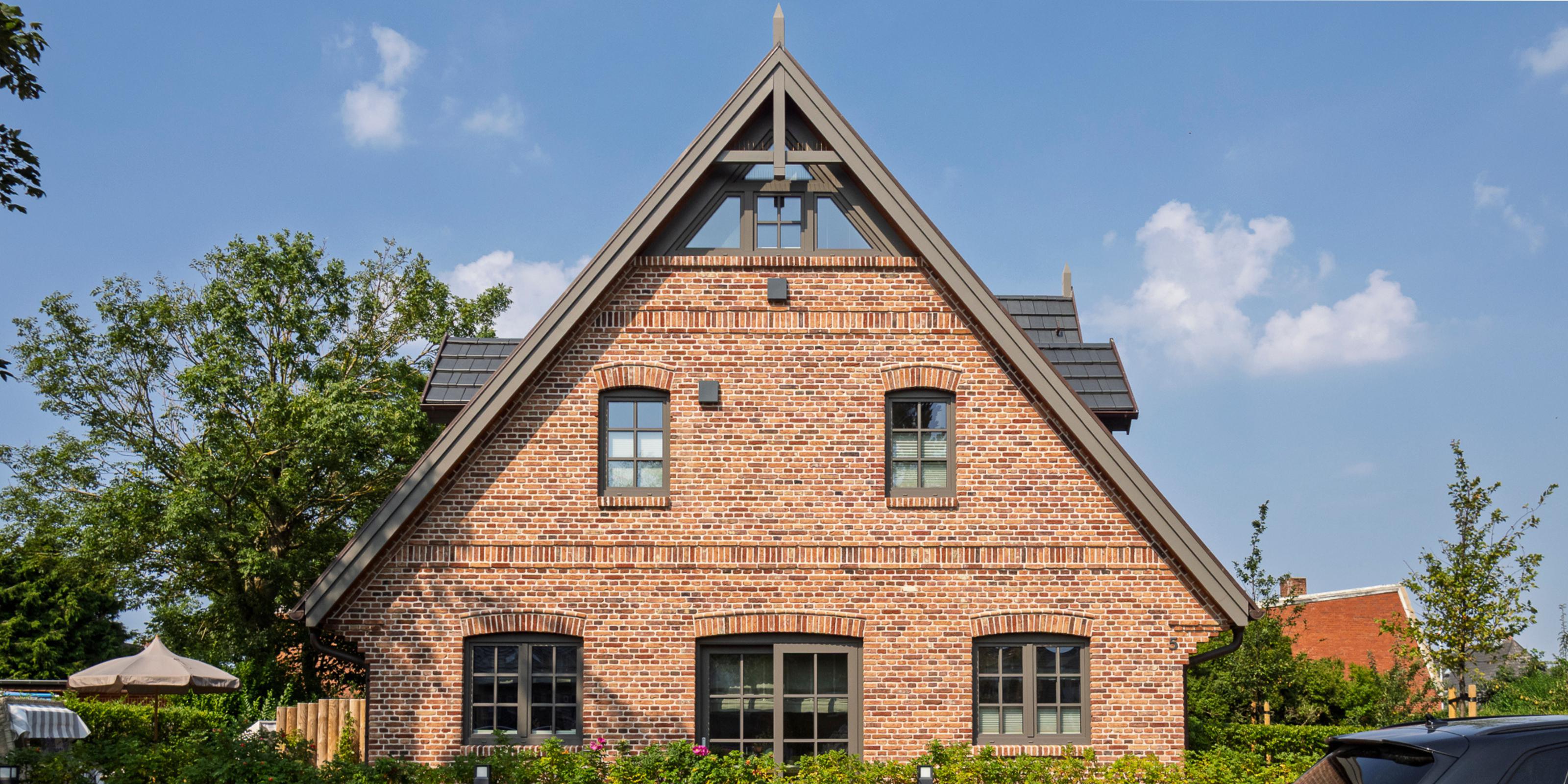 Außenansicht des charmanten Ferienhauses 'Greta & Sylt' im traditionellen Backstein-Stil unter blauem Himmel.

