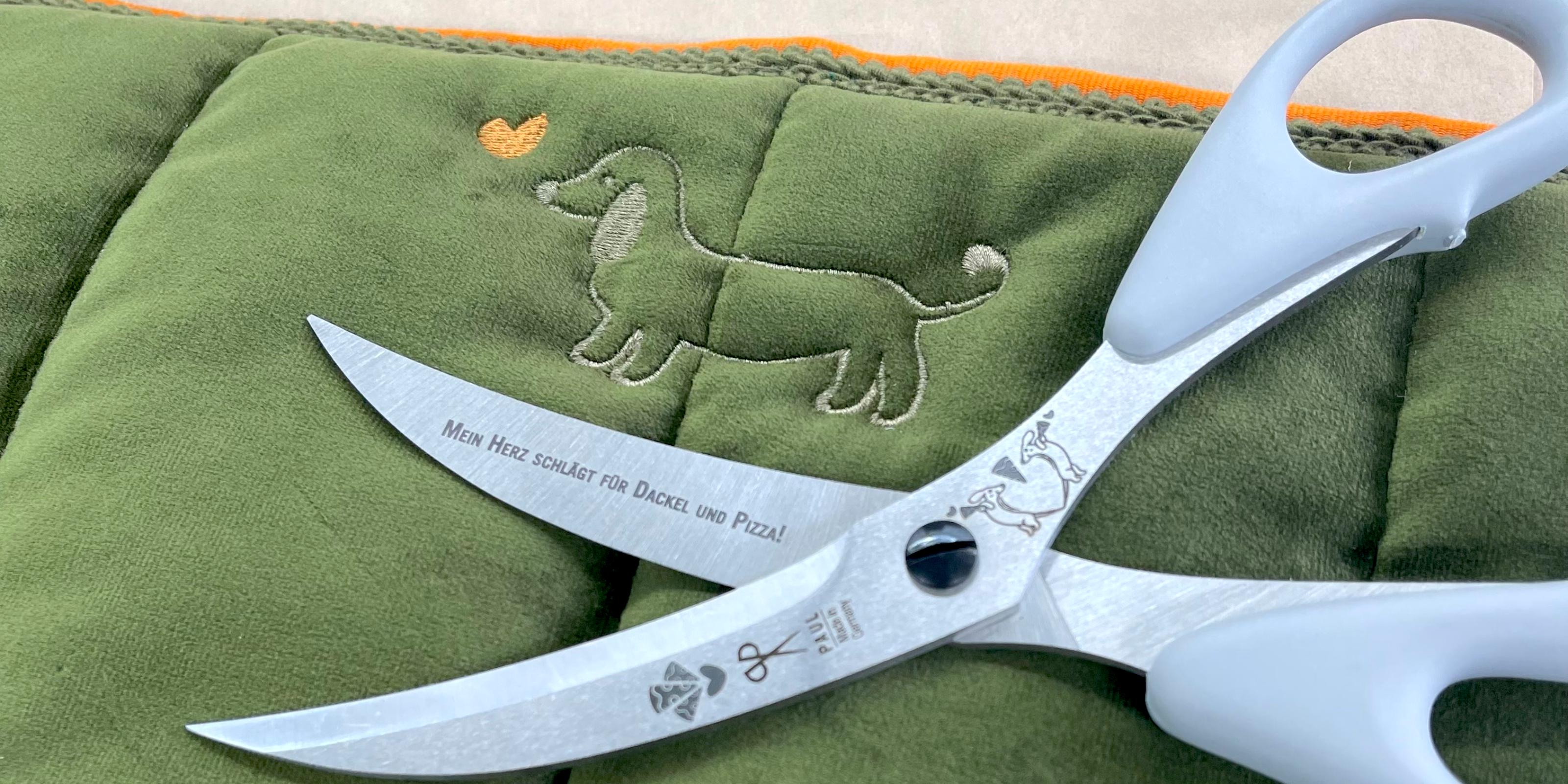 Kategoriebild: Dackel-Schere mit Gravur "Mein Herz schlägt für Dackel und Pizza!" auf einer grünen Hundedecke.
