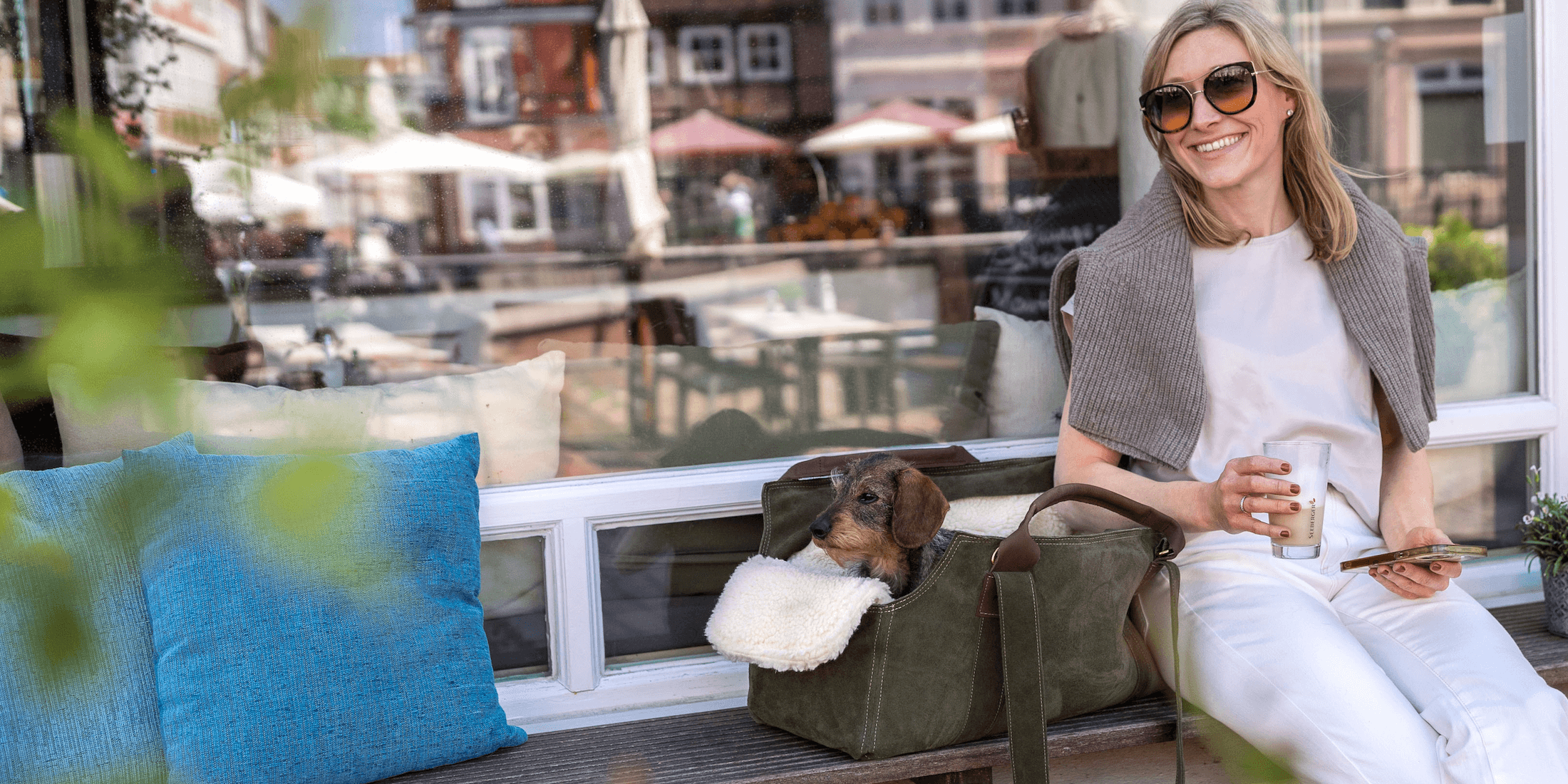 Newsletter-Banner: Gründerin Julia entspannt mit Dackel Gretchen in einer Greta & PAUL Hundetasche vor einem Café.
