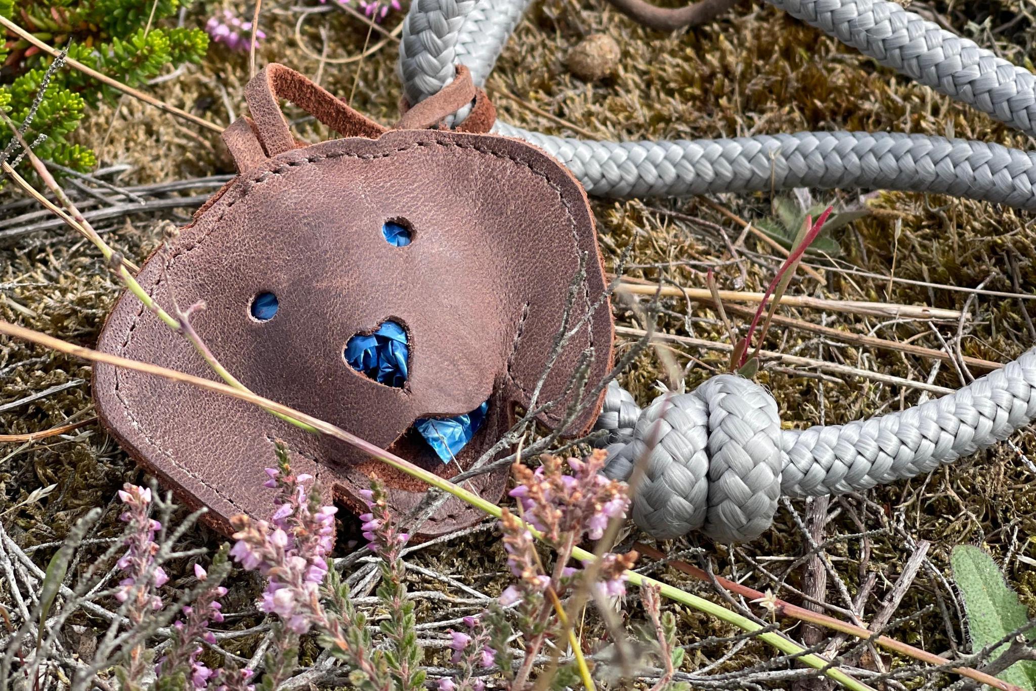 Hochwertiger Tütchenspender 'Theo' aus Leder in Form eines Hundekopfes, befestigt an einer blauen Tauleine.

