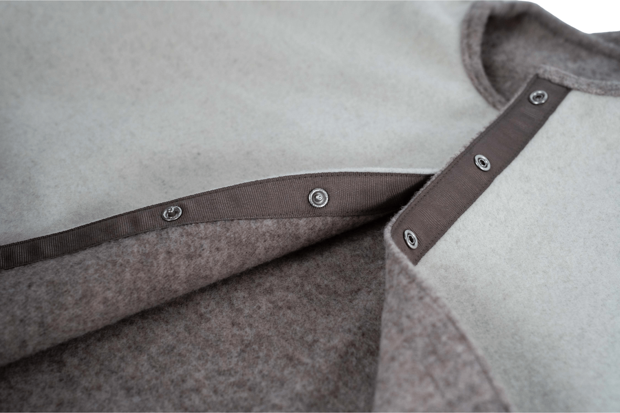 Detailaufnahme des vorderen Druckknopfverschlusses des Wendecapes Gretchen Couture in Beige-Wollweiß mit zweilagiger Wollverarbeitung.